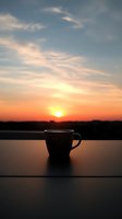 Silhouette of coffee cup against dramatic sunset sky with orange and pink hues, creating peaceful morning or evening atmosphere for lifestyle and relaxation concepts.