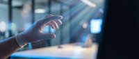 Hand reaching toward glowing holographic sphere in modern office environment with soft lighting and blurred background for technology presentations.