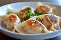Pan-fried dumplings garnished with fresh herbs served on white ceramic plate, golden brown crispy bottoms and tender wrappers filled with savory meat mixture.