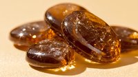 Amber colored translucent vitamin supplement capsules with liquid omega oils inside on beige background with soft shadows and reflective surface. Medical healthcare concept.
