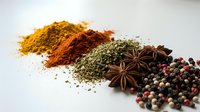 Colorful spices and herbs scattered on white background including turmeric, paprika, oregano, star anise and peppercorns for cooking and seasoning.