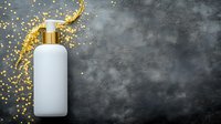 White cosmetic bottle with golden splash and glitter on dark concrete background, mockup for skincare product packaging and luxury beauty branding.