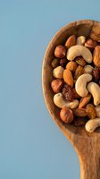 Mixed nuts and dried fruits in wooden spoon on blue background. Healthy snacking, protein rich foods, natural nutrition ingredients for cooking and baking.