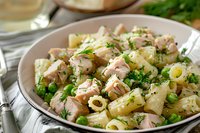 Creamy pasta salad with tender chicken pieces, rigatoni, fresh green peas, and herbs in light mayonnaise dressing served in ceramic bowl, close up view of homemade meal.