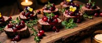 Gourmet beef canapes with cranberry sauce and fresh herbs on rustic wooden board, elegant appetizers for holiday entertaining and fine dining occasions.