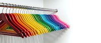 Colorful rainbow hangers arranged on metal rod creating vibrant spectrum from red to purple for wardrobe organization and closet storage solutions.