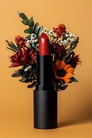 Red lipstick with autumn flowers arrangement on orange background. Creative cosmetic product photography for beauty and makeup advertising campaigns.