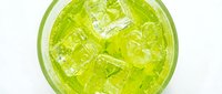Refreshing green cocktail with ice cubes and mint leaves in a glass, top view on white background, perfect for menu and beverage concepts.