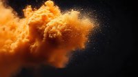 Orange powder explosion on black background creating dynamic cloud formation with floating particles and dramatic lighting effect.