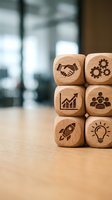 Wooden business concept blocks with engraved icons including handshake, gears, growth chart, team, rocket and lightbulb stacked on office desk for strategy planning.