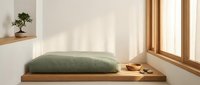 Minimalist wooden platform bed with green cushion in sunlit room featuring natural wood window frame and small bonsai tree on floating shelf.