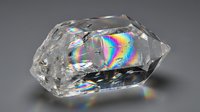 Clear crystal quartz gemstone with rainbow light refraction displaying prismatic spectrum colors on neutral background for jewelry design.
