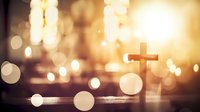 Wooden cross silhouette against blurred golden bokeh lights background creating spiritual atmosphere for religious and faith concepts.