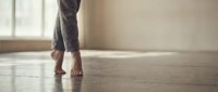 Woman walking barefoot on wooden floor in bright room with natural light from window creating peaceful morning atmosphere at home.