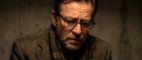 Serious mature Caucasian businessman with glasses and beard in brown suit jacket looking contemplative in dimly lit office setting for corporate concepts.