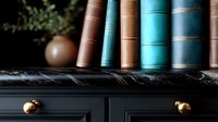 Vintage hardcover books in brown and turquoise colors arranged on black marble shelf with brass knobs, creating moody literary atmosphere for home library decor.
