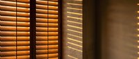 Warm sunlight filtering through wooden window blinds creating striped shadow patterns on interior wall. Natural lighting and home decor concept.