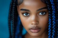 Close up portrait of young African American woman with blue braids and striking blue eyes against turquoise background, beauty and fashion concept.