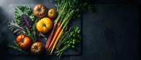 Fresh organic vegetables including heirloom tomatoes, carrots, and leafy greens arranged on dark slate board for healthy cooking and farm-to-table cuisine.