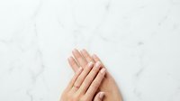 Manicured hands with natural nails displayed on white marble surface, showcasing nail care and beauty treatments for cosmetics and wellness marketing.