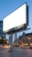 Blank white billboard on urban street at dusk with illuminated buildings and pedestrians, suitable for advertising mockups and commercial campaigns.