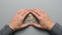 Mature male hands protecting pile of coins on gray background, representing financial security, savings, and wealth protection concept.