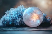 Frozen soap bubble with delicate frost patterns glowing in sunset light against blue hydrangea flowers on dark background, magical winter macro photography.