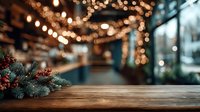 Festive wooden table with pine branches and berries against blurred restaurant interior with warm string lights creating cozy holiday atmosphere.