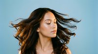 Young woman with flowing brown hair in motion against blue background, eyes closed in peaceful expression, natural beauty and freedom concept.