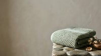 Folded knit sweaters stacked with decorative wooden beads on neutral textured background, suitable for home decor, fashion, and lifestyle design projects.