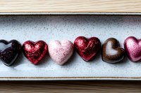 Colorful chocolate hearts in metallic foil wrappers arranged in row on white ceramic plate. Romantic confectionery composition for Valentine's Day celebration.