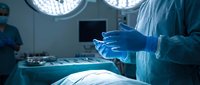 Surgeon in blue gloves preparing for operation in modern operating room with surgical lights and medical equipment for healthcare procedures.