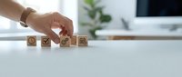 Hand arranging wooden cubes with business icons on white desk, symbolizing strategy, planning, and workflow management in a modern office.