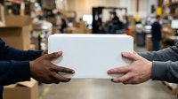Two workers holding blank white card in warehouse environment with industrial background and shelving.