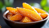 Caramelized orange segments glazed with honey in brown ceramic bowl, close up view against dark background with soft bokeh effect and fresh herbs.