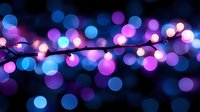 Glowing string lights creating magical bokeh effect in blue and pink colors against dark background, festive holiday atmosphere with defocused light circles.
