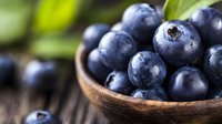 Fresh ripe blueberries in wooden bowl on rustic table, macro shot with selective focus. Natural organic berries with water drops and green leaves.