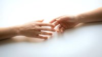Two hands reaching toward each other in gentle connection against clean white background symbolizing support, unity and human touch.
