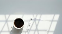Overhead view of white mug with black coffee and measuring tape on bright surface with window shadows, suitable for business, productivity, and lifestyle design projects.