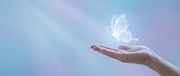 Open hand releasing glowing white butterfly against soft pastel sky background symbolizing freedom, transformation and spiritual growth.