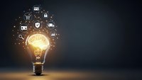 Glowing light bulb with digital business icons floating above representing innovation, technology solutions, and creative ideas for modern enterprises.