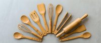 Wooden kitchen utensils arranged in a fan shape on a gray surface, including spoons, spatulas, a whisk, and a rolling pin.