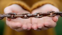 Rusty metal chain held gently in open palms against blurred natural background, symbolizing freedom, connection, and breaking barriers. Metaphor for relationships and bonds.