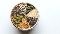 Assorted healthy seeds and legumes arranged in wooden bowl including sunflower seeds, pumpkin seeds, chia seeds, quinoa and beans for nutrition.
