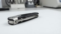 Modern black multi-tool knife with stainless steel components on white kitchen counter surface for everyday carry and outdoor activities.