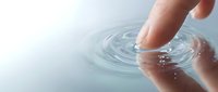 Adult hand touching calm water surface creating concentric ripples and waves in soft light, suitable for wellness, spa, skincare, and relaxation concepts.