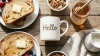 Cozy morning breakfast flat lay with toast, butter, berries, granola, honey jar, and a white mug on rustic wooden table.