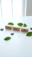 Wooden blocks spelling EARTH DAY with leaf symbol surrounded by fresh green leaves and stones on white surface for environmental awareness campaigns.
