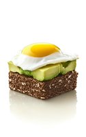 Healthy breakfast toast with dark seeded bread, sliced avocado and sunny side up egg on white background, isolated food photography for menu design.