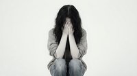 Young woman covering face with hands in despair sitting on floor expressing grief depression anxiety stress mental health struggles emotional pain.